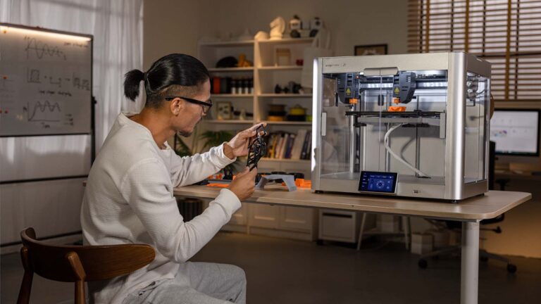 A person examines a printed object while seated next to a Snapmaker J1s 3D printer.