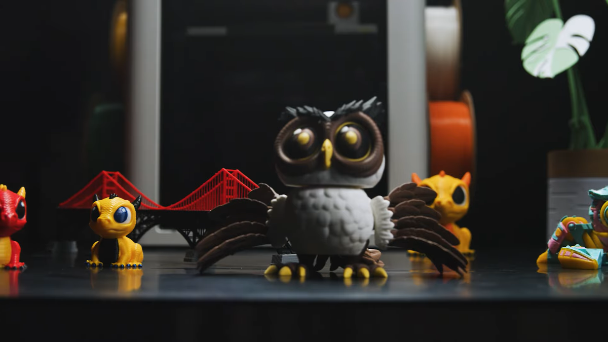 A collection of intricate, multi-color 3D printed models, including a detailed owl and a red bridge, demonstrates the high-quality results of advanced printing.