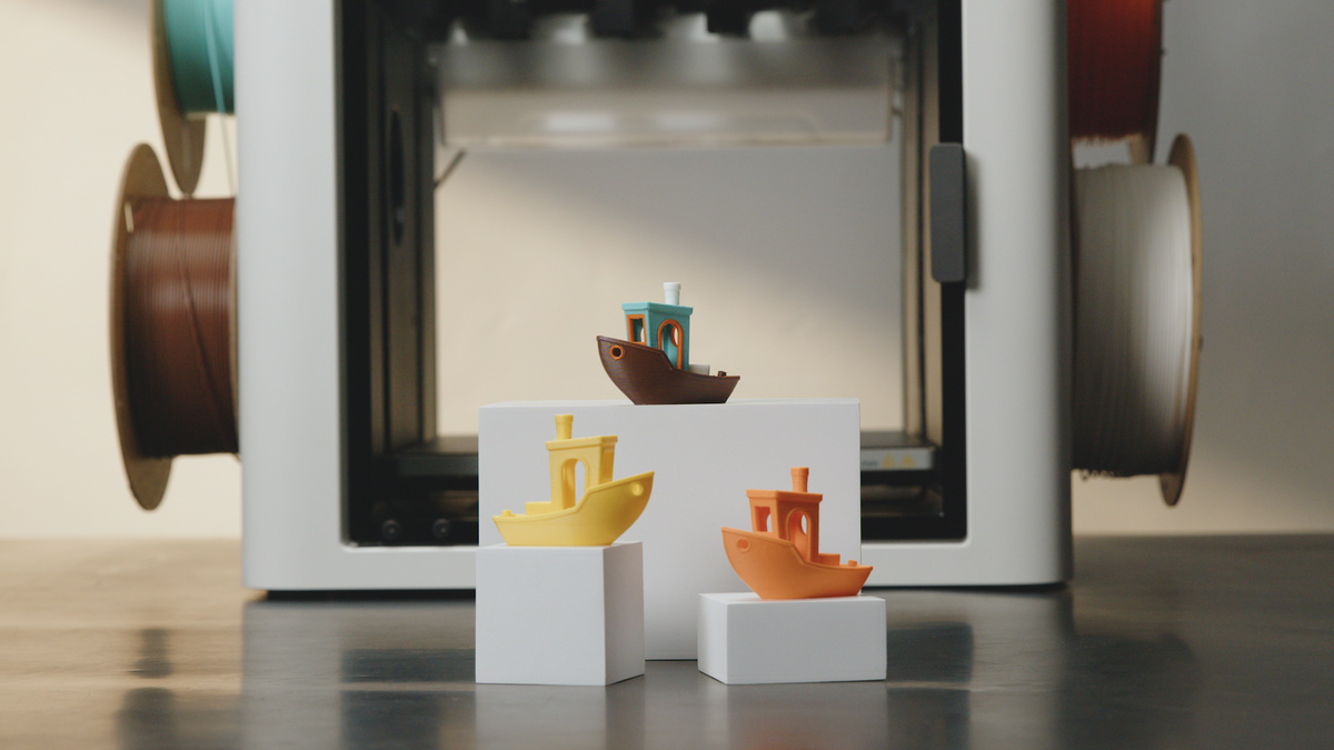 Three colorful 3D printed Benchy boats displayed on pedestals in front of a Snapmaker U1 printer, showcasing multi-color printing capabilities.