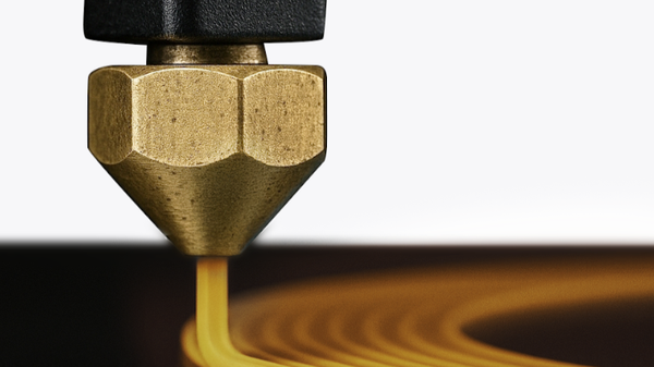 A close-up of a brass 3D printer nozzle extruding yellow filament onto a dark print bed.