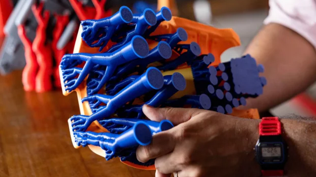A user holds a finished 3D print to demonstrate the intricate branching structure of blue tree supports attached to the model.