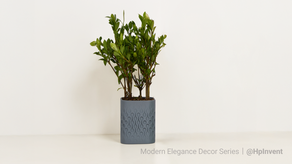 A modern, square 3D printed planter in grey with a wavy, geometric pattern, holding a small green plant on a white shelf.
