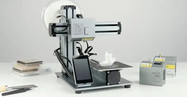 Modular desktop 3D printer with filament spool and accessory modules on a white workbench - modern additive manufacturing machine.